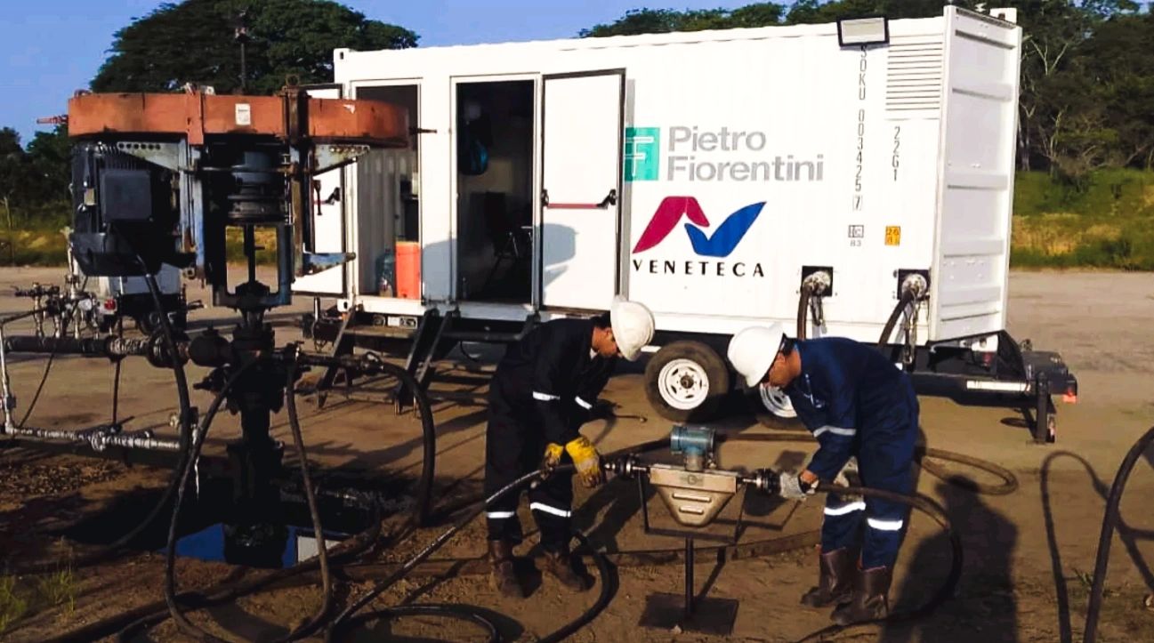 Two workers in protective gear operate equipment near a Pietro Fiorentini Veneteca trailer.