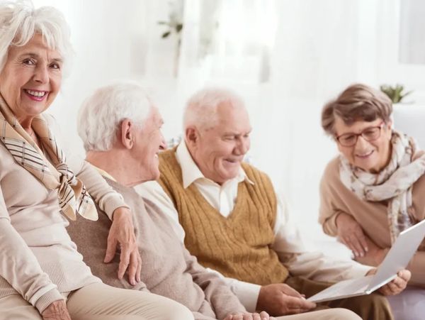 a group of elderly people smiling and sitting together on a couch and talking