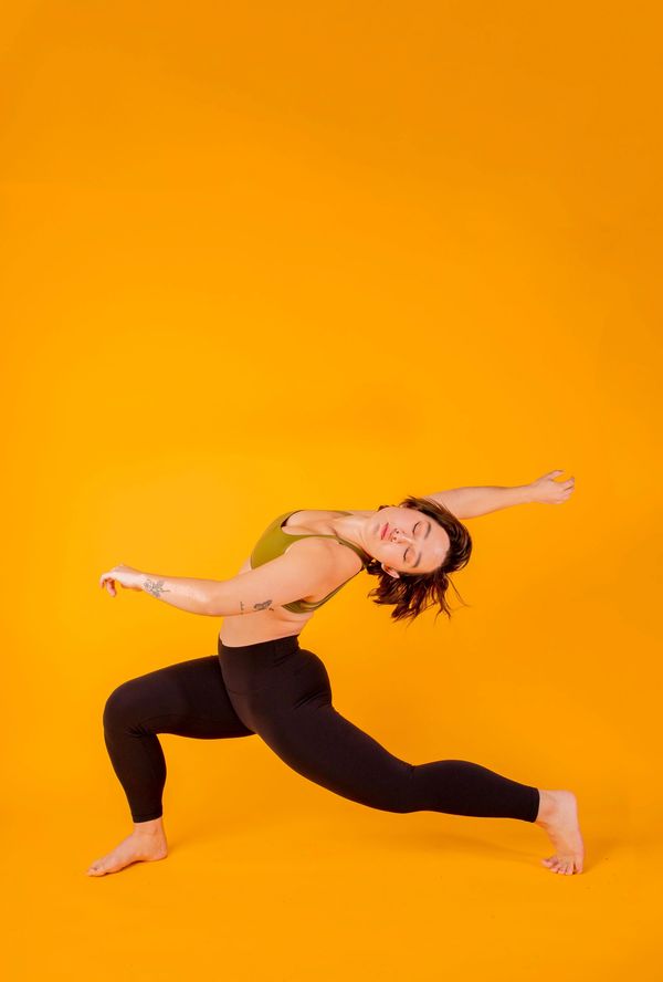 A woman gracefully poses in a yoga stretch against a vibrant orange background.