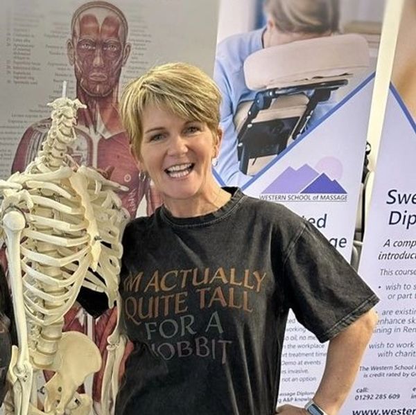 Smiling woman stands next to a skeleton model in an educational setting.