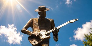 Metal statue of a guitarist against a sunny sky.