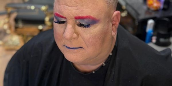 Sissy Bitch Mark Moran in Gardner KS with makeup of pink eyebrows, false eyelashes, black cape