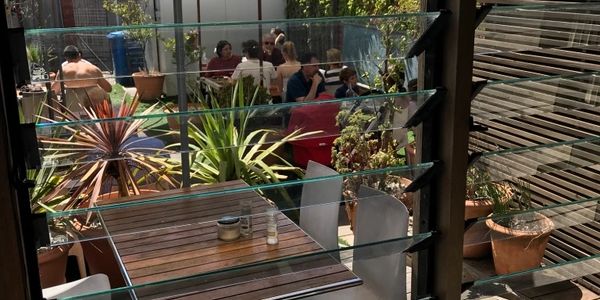 People dining outdoors in a sunny garden patio with plants.