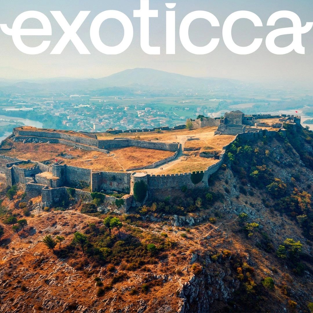 Aerial view of an ancient fortress on a rocky hill with a town in the background.