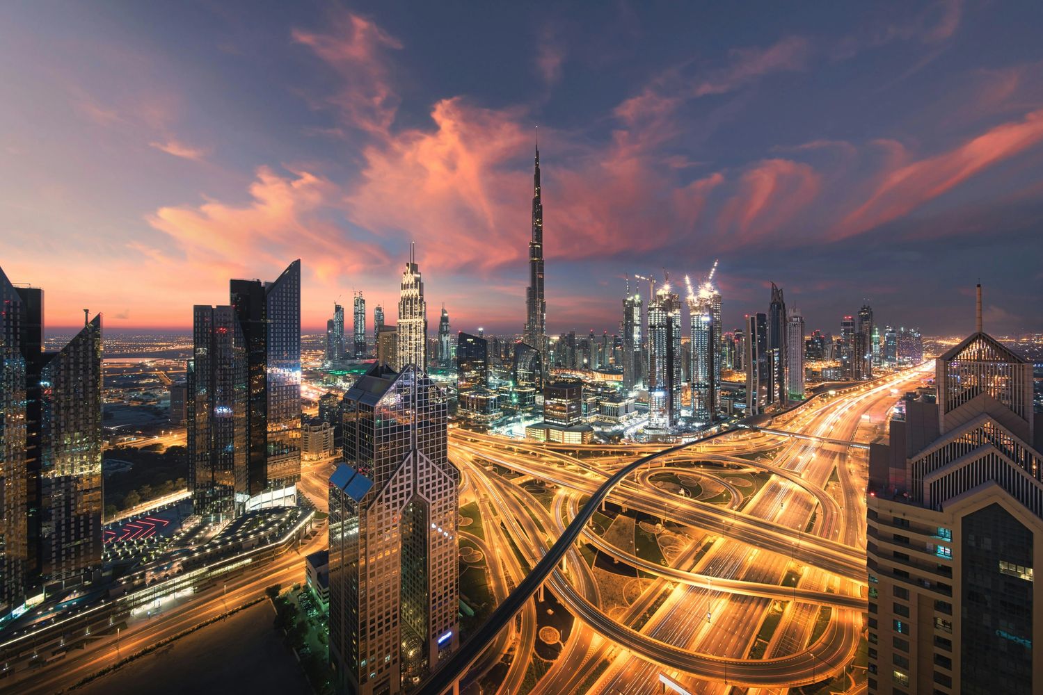 Dubai skyline at sunset with illuminated highways and Burj Khalifa.