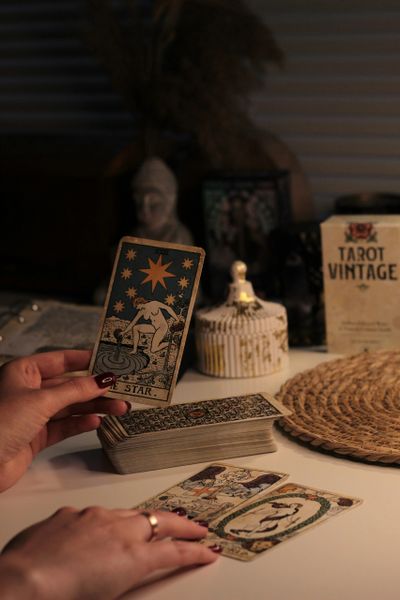 Hand holding The Star tarot card from a vintage deck on a cozy table.