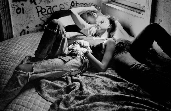 Two people relaxing on a bed in a grungy room.