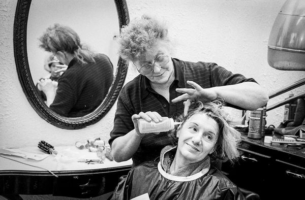 Older woman applying hair treatment to a younger woman in a salon.