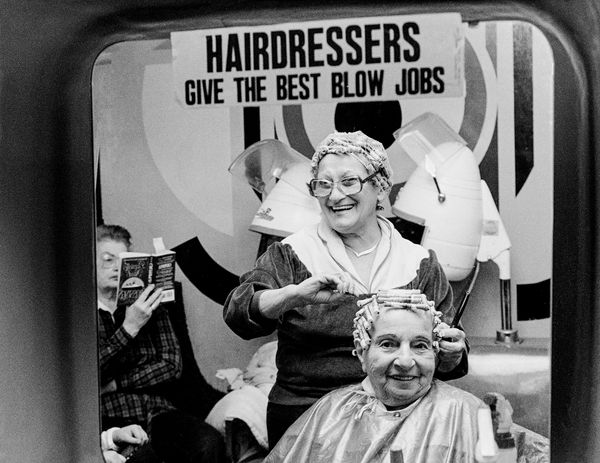 Hairdresser curling a client's hair under a sign with a pun.