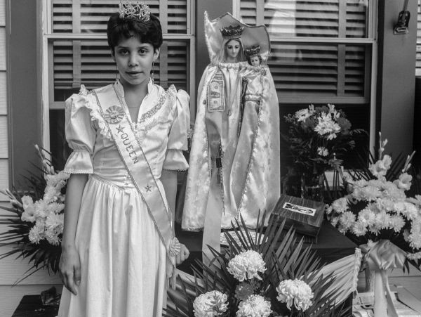 Portrait of a girl in a queen costume with religious statues and flowers.