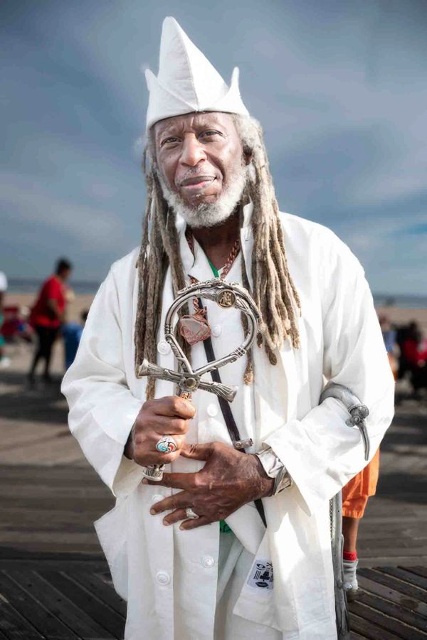 Elderly man in white attire holding a decorated staff.
