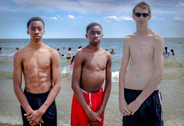 Three young men standing at the beach, shirtless.
