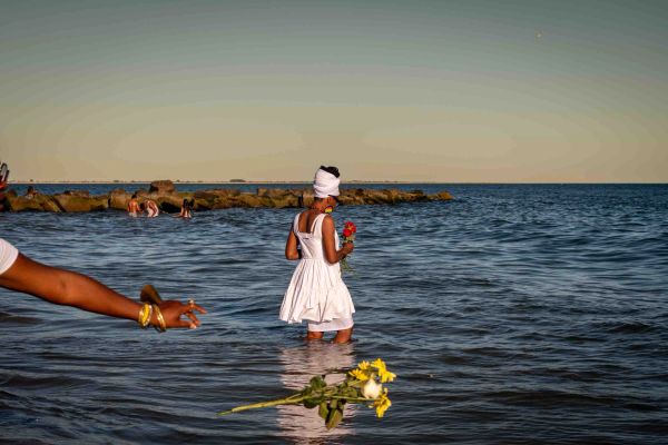 Woman in white dress standing in water holding flowers.