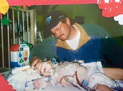 A man tenderly watches over a child in a hospital bed with medical tubes.