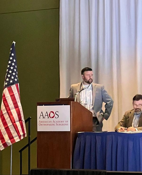 Speaker at American Academy of Orthopaedic Surgeons conference with U.S. flag.