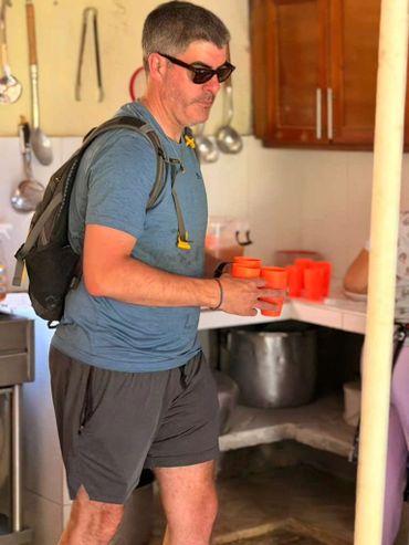 Man with backpack holding orange cups in a kitchen.