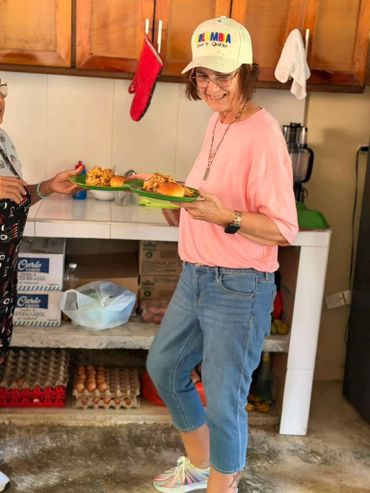 Woman smiling while holding plates of food in a kitchen.