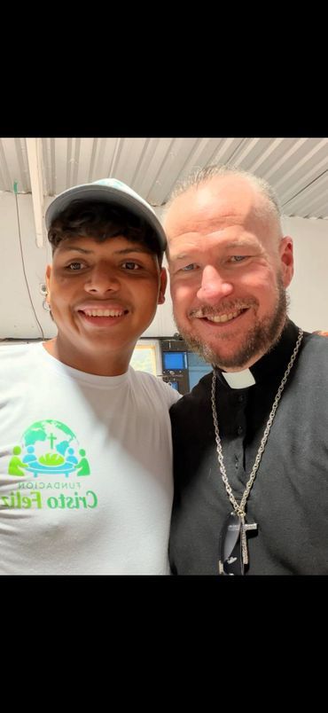 Two men smiling together, one wearing a religious collar and cross.