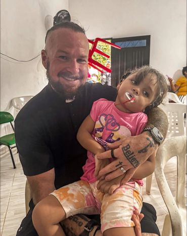 Man holding a young girl with a pacifier, both smiling gently indoors.