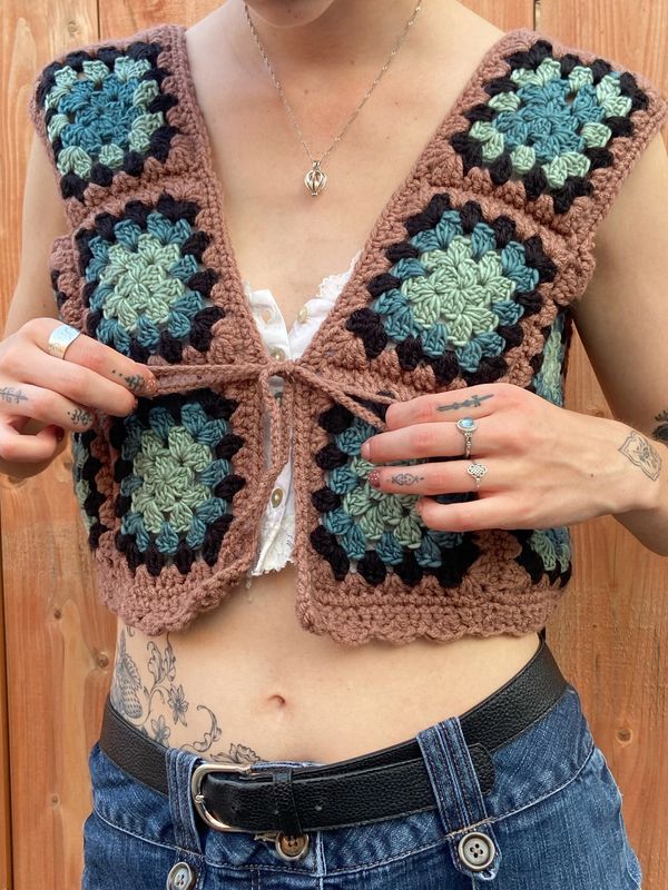 Crocheted vest with square patterns worn over a white top and denim jeans.