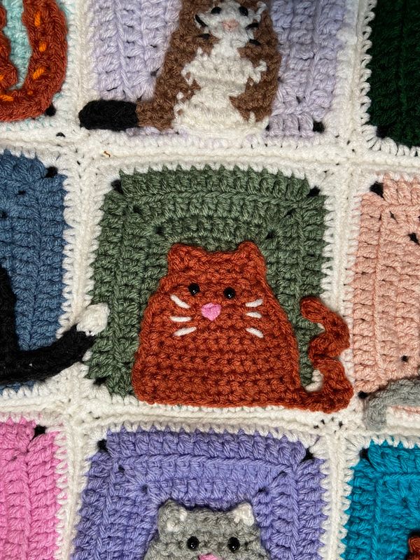 Crocheted blanket squares featuring cute cats in different colors and patterns.