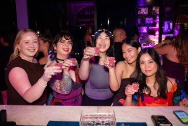 Five friends cheer with colorful drinks at a lively bar.