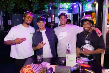 Four friends posing happily at a restaurant table with food and drinks.