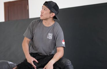 Man sitting wearing a backwards cap and grey T-shirt.