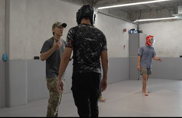 Three men in a martial arts gym, one wearing a red helmet.