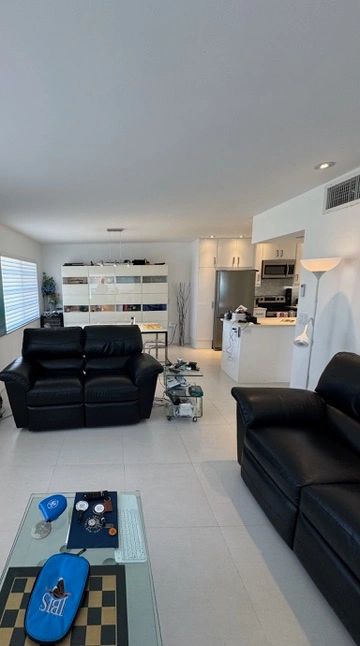 Modern living room with black leather sofas and white kitchen in the background.