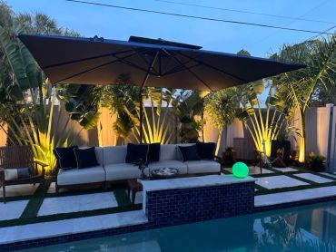 Outdoor seating area with large umbrella and illuminated plants.