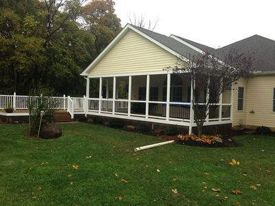 The back of a house with cream vinyl siding. It features a cathedral gable roof a screened in back p