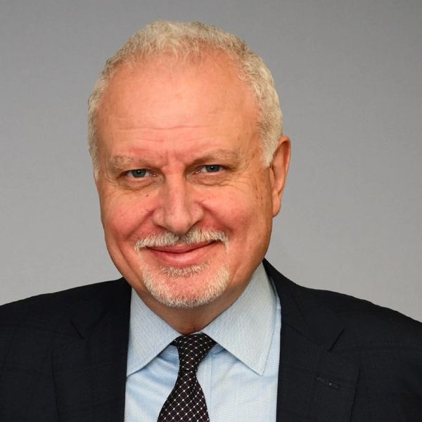Smiling older man with gray hair and beard in business attire.