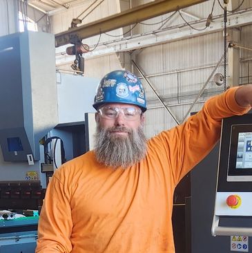 Worker in orange shirt and safety helmet posing in industrial setting.