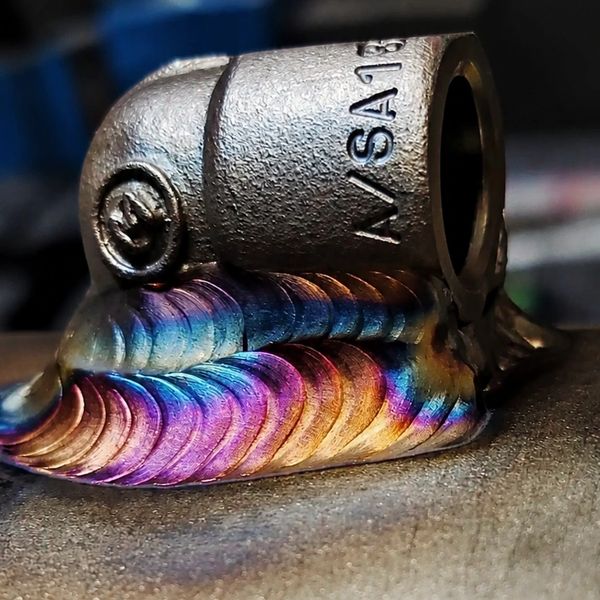 Close-up of a colorful, precision TIG weld on a metal pipe fitting.