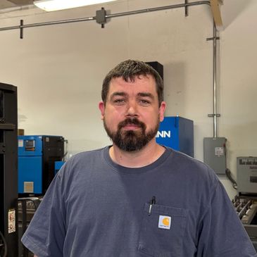 Man with beard in a workshop wearing a navy blue shirt.
