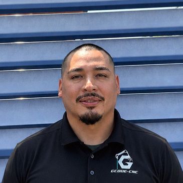 Man in black polo shirt with GCode CNC logo standing in front of blue horizontal slats.