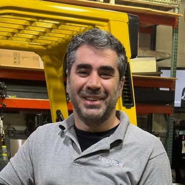 Smiling man in a gray polo shirt in an industrial workspace.