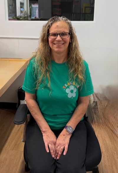 Smiling woman with glasses sitting in an office chair, wearing a green shirt.