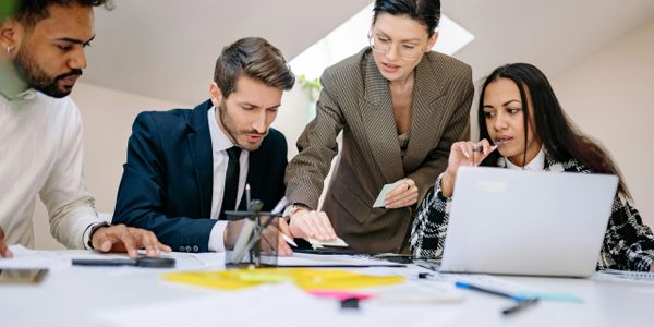 Four colleagues collaborating intensely over documents and a laptop in a bright office.