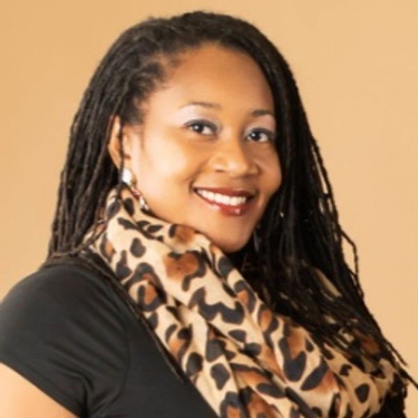 Smiling woman with long dreadlocks wearing a leopard print scarf and black top.
