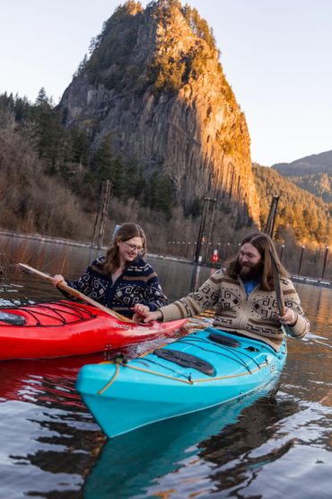Couple holding hands while kayaking near a rocky mountain at sunset.
