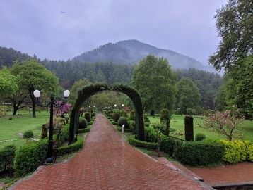 A serene garden pathway leading through an archway with lush greenery and mountains in the background.