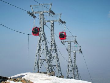 Red cable cars moving on metal towers over snowy mountain.