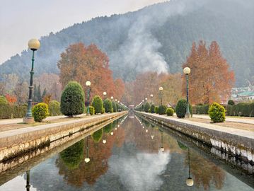 Symmetrical garden pathway with lamps and autumn trees reflected in water.