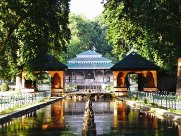 A serene garden with symmetrical water features and traditional architecture surrounded by lush trees.