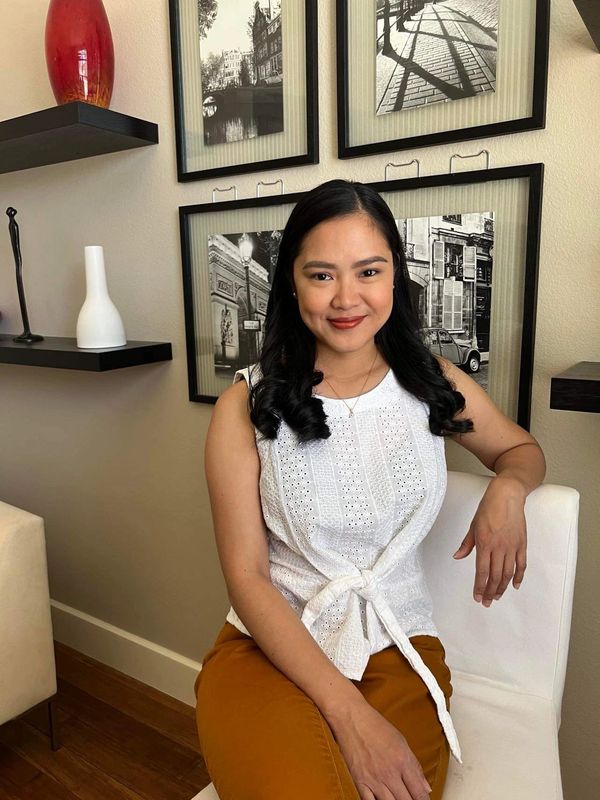 Woman with curled hair sitting on a white chair in a cozy room with framed black and white photos.