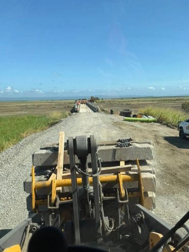 Construction equipment moving concrete slabs on a rural road.