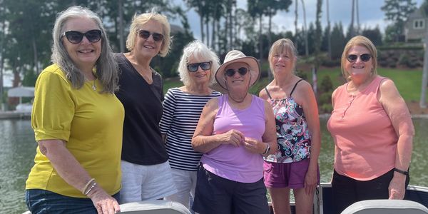 Group of six women smiling by a lakeside.