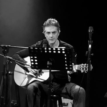 Siyah beyaz müzik performansı, gitarla adam mikrofon önünde.